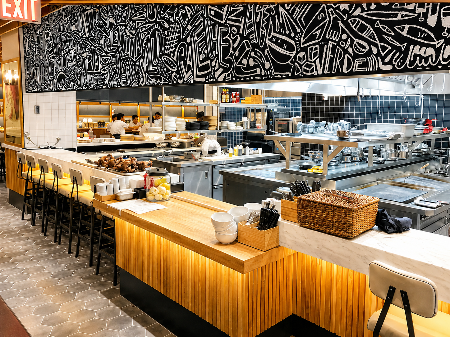 Open-concept restaurant kitchen with wood counter, bar seating, and stainless steel workstations.