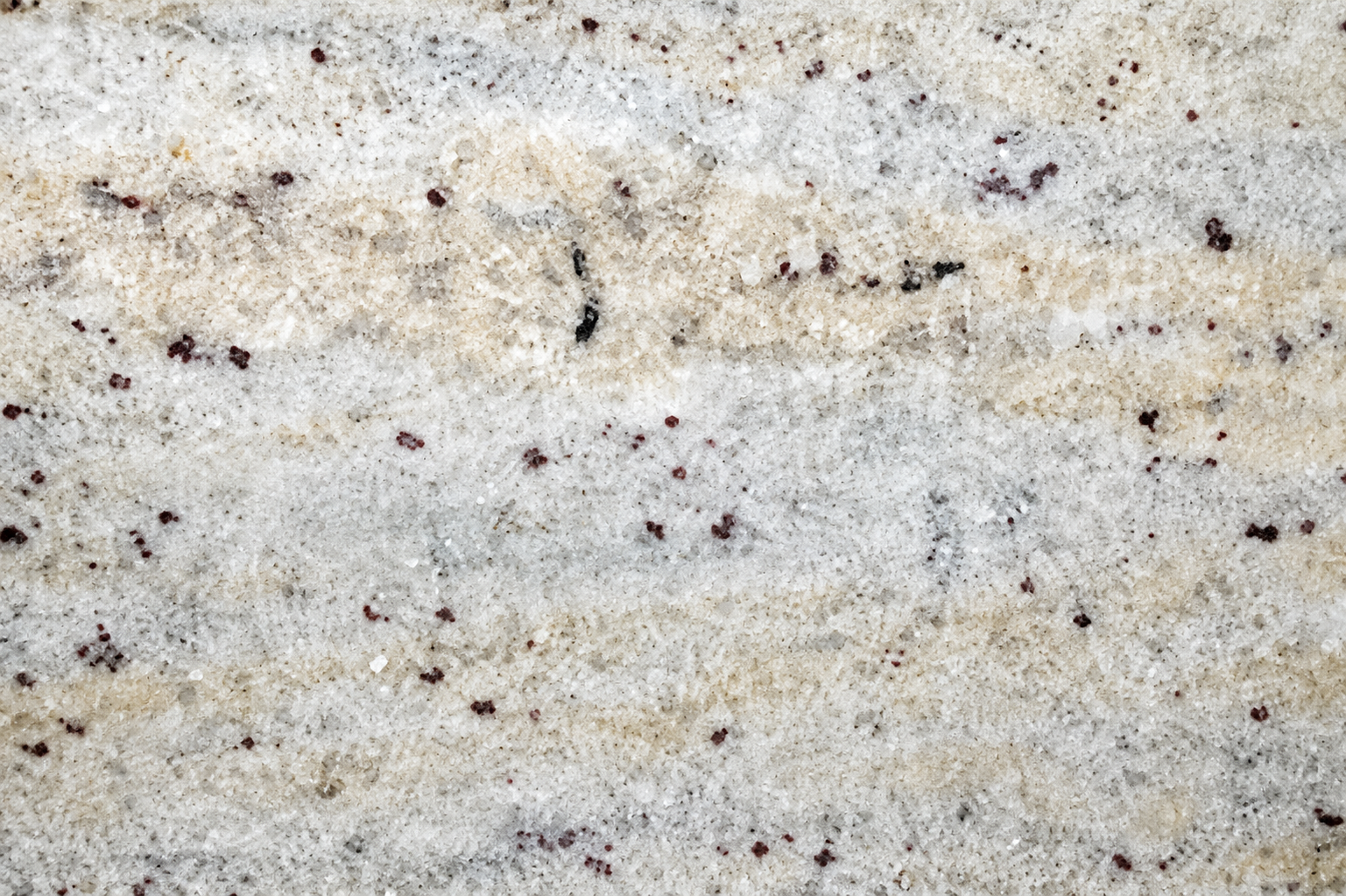 Close-up of cream and white granite with subtle veining and burgundy mineral flecks.